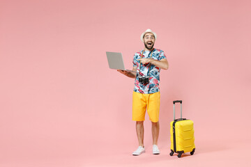 Full length of excited young traveler tourist man pointing index finger on laptop pc computer...