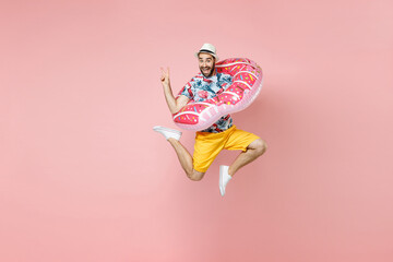Full length funny traveler tourist man in summer clothes hat jumping hold inflatable ring showing victory sign isolated on pink background. Passenger traveling on weekends. Air flight journey concept.