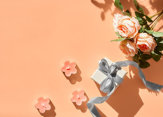 Spring composition with flowers and gift box with ribbon on pastel peach background. Greeting card for spring holiday Birthday, Woman or Mothers Day.