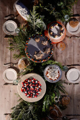 Decorated festive wooden table with white cake, cupcake, pie. Christmas decor of berries, thuja branches and a Christmas tree, sprinkled with snow. View from above