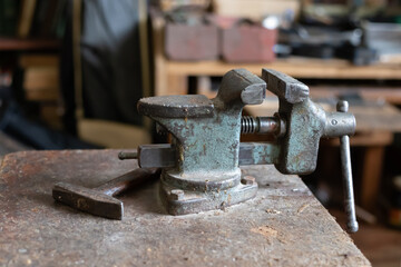 An old vise is on the table. There is a hammer next to them.