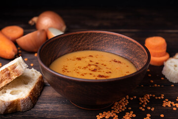 Hot red lentil cream soup on a dark wooden table.