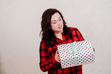 Attractive woman in a red checkered dress with a gift against the white wall. 