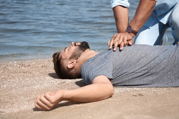 Passerby performing CPR on unconscious young man near sea. First aid