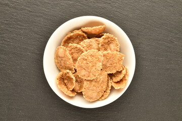 Natural multi-grain flakes in a white ceramic plate on a slate board, close-up, top view.