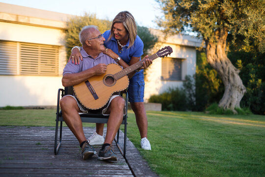 anziano signore canta una canzone alla moglie con la chitarra acustica nel giardino di casa
