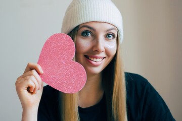 Beauty portrait of smiling blonde young woman with pretty pink heart. Big paper heart in the hands.Cupid day. - 407721666