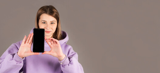 Portrait of a happy casual woman showing blank smartphone screen isolated on a gray background