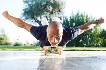 Uomo cinquantenne con maglia nera e pantaloncini chiari va sullo skateboard in posizione prona - obrazy, fototapety, plakaty