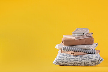 Stack of clean bed linen and pillow on yellow background. Space for text