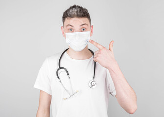 Male doctor in medical uniform points his fingers at a medical mask on his face. Concept of protection and prevention of covid-19, colds and flu