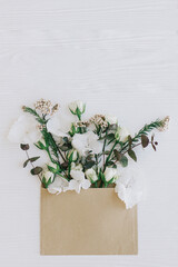 Hello spring. Roses, hydrangea, and eucalyptus branches growing from craft envelope on white wood