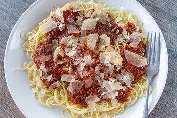 Plate of spaghetti with meat sauce with large shaved parmesan cheese