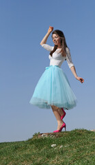 Naklejka na ściany i meble A girl in a blue skirt and pink shoes stands against the blue sky