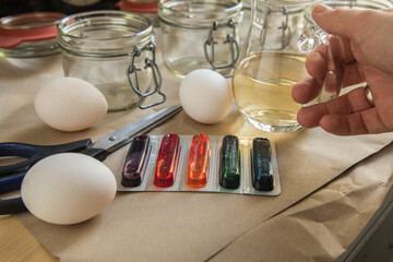 Frau mit Essig, Wasser und bunten Ostereier Kaltfarben in Rot, Orange, Gelb, Blau, Grün in Verpackung auf Papier Unterlage mit Gläser, gekochte Eier und Schere zum Färben zu Ostern