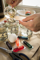 Frau mit Löffel, Essig, Wasser und bunten Ostereier Kaltfarben in Rot, Orange, Gelb, Blau, Grün in Verpackung auf Papier Unterlage mit gekochte Eier und Schere zum Färben zu Ostern