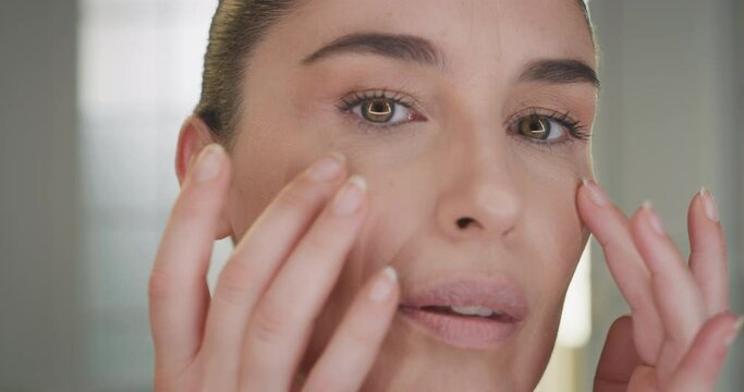 Beauty shot of mature woman with perfect face skin after applying moisturizing cream pampering it gently with fingers to absorb better on golden background. Concept of skincare, cosmetics, healthcare