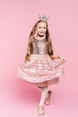 full length of cheerful little girl in dress and crown posing on pink © LIGHTFIELD STUDIOS