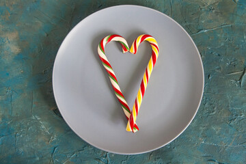 Obraz premium Colorful Christmas candy canes lying on the gray plate in the shape of a heart. The concept of Valentine's Day