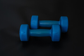 Two blue dumbbells for fitness lie in parallel on a black background