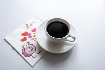 White cup of coffee stands on a saucer and on a napkin with hearts on a white background