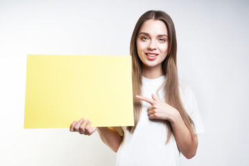 Fototapeta premium A beautiful blonde in a white T-shirt on a gray background holds a yellow sign