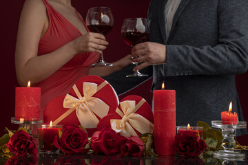 A man in a jacket and a woman in a pink dress are holding hands. Candles and luxury roses, gift boxes in the shape of a heart with satin bows. Cropped view, Valentine's Day Engagement