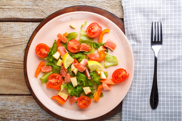 Salad with salmon and cherry tomatoes in a plate on a wooden table on a wooden stand stand next to a fork and napkin.