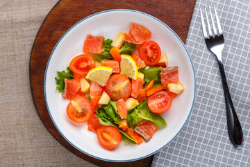 Salad with cold salmon and cherry tomatoes in a plate on a gray background on a wooden stand a stand next to a fork.
