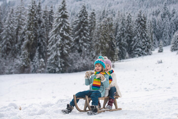 Happy children in snow. Two kids ride on a wooden retro sled on a winter day. Active winter outdoors games. Happy Christmas vacation concept.