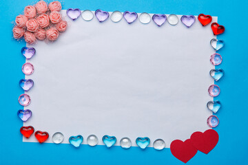 In a frame made of pebbles of hearts, a white copy space on a blue background and a bunch of decor in the corner.