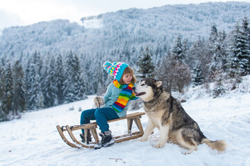 Happy winter child boy. Dog alaskan malamute and kid in snow winter, Austria or Canada.