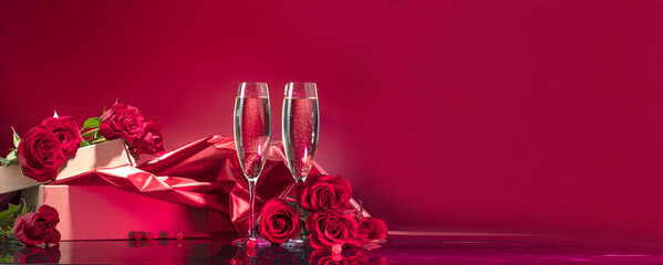 Luxurious glasses with sparkling wine open box with glitter brocade surrounded by selected roses on a mirror surface on a red background. Valentine's day or romantic evening invitation