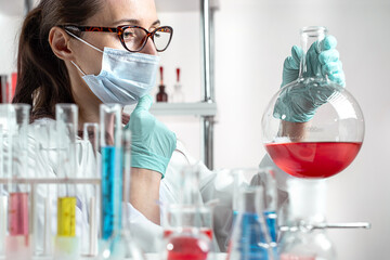 Woman chemistry laboratory assistant looking at colored liquid in laboratory glass.