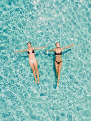 Couple of woman floating in clear blue sea. Aerial view