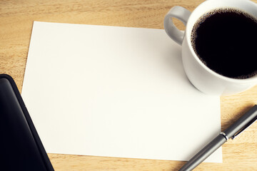 Blank paper on wooden desk table with cup of coffee, pen and smartphone. Mock up template