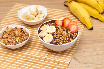Delicious açai bowl, on wooden table, with banana and strawberry. Granaola pot.