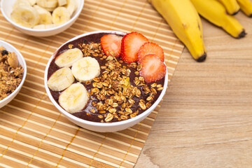 Açai bowl with banana and strawberry on wooden table.