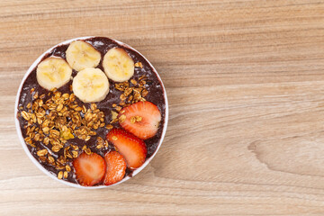 Brasilerio açai ice cream bowl, with banana, strawberry and granalo, to the left of the image, with space for text.