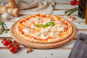 Pizza with slices, sauce and herbs, wooden white background