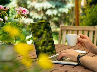 Man works on laptop in the garden and drink coffee. Home office with relax and nature. Freelancer...