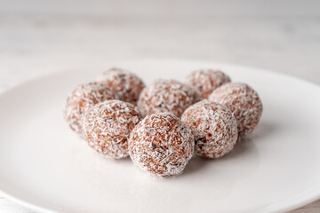 Truffles made from dates and coconut shavings are laid out on a white plate in close-up