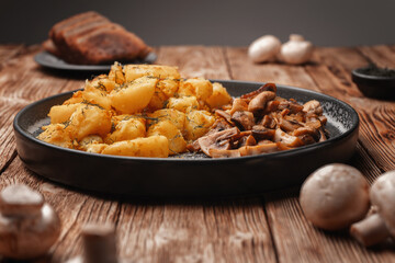 Vegetarian fried potatoes with mushrooms on a concrete plate on a wooden plank table.