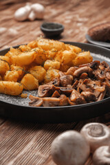 Fried potatoes with mushrooms on a gray plate near fresh mushrooms, close-up