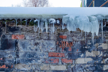 Closeup background of icicles hanging off the roof of an old house with a worn brick wall with copy...