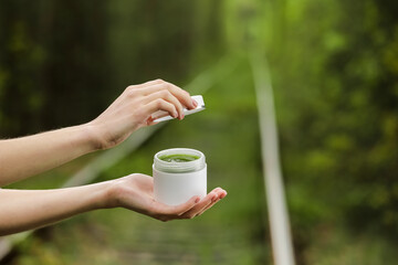Young Female hands open a white jar of cream for face or body. organic natural skincare products on green natural background. Packaging of lotion or cream. Beauty cosmetic skin care concept.