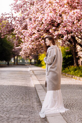 woman's day. beautiful young woman in luxury long dress near blossoming of sakura. stylish girl near blossoming sakura flowers on background in the spring park. Harmony with nature concept