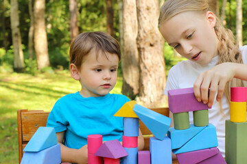 A girl plays with a small boy in colorful cubes in nature in summer in sunny weather.