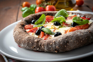 Deliziosa pizza con impasto a base di cereali e condita con pomodorini, mozzarella, olive e...