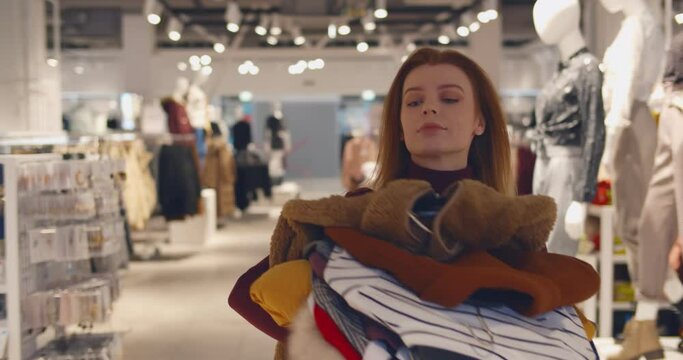 Young woman with pile of clothes walking to fitting room in clothing store